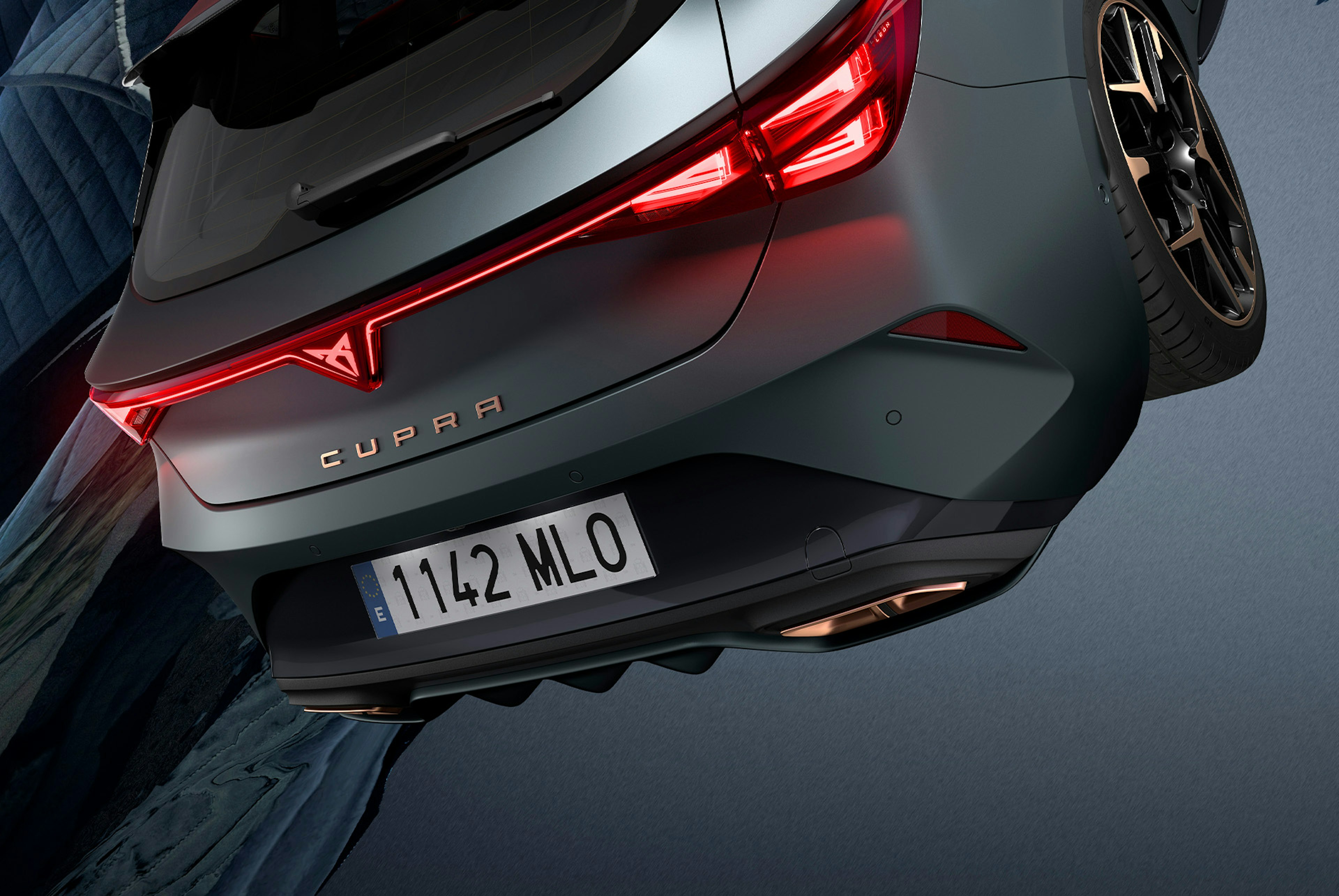 Technologie de la nouvelle Cupra Leon 2025 hybride, éclairage arrière LED, véhicule hybride rechargeable garé sur du ciment, structure avec des bords brillants. Le véhicule est présenté dans une finition gris mat avec des jantes forgées copper/black.